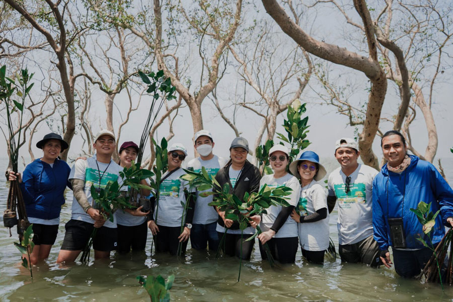 happy onsemi employees standing in water and holding plants.